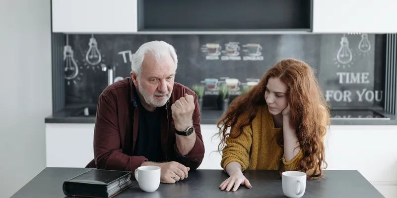 Two people talking across a kitchen table over coffee