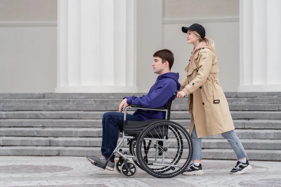 A support worker walking outdoors with a young man in a wheelchair