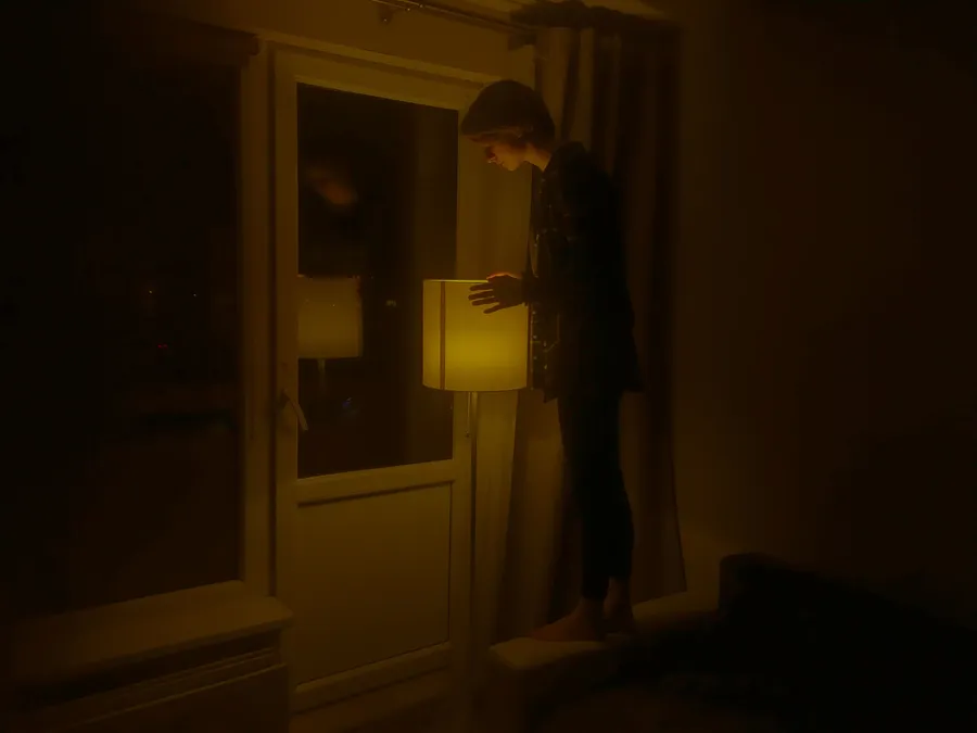 A person standing beside a lamp in a dimly lit room at night