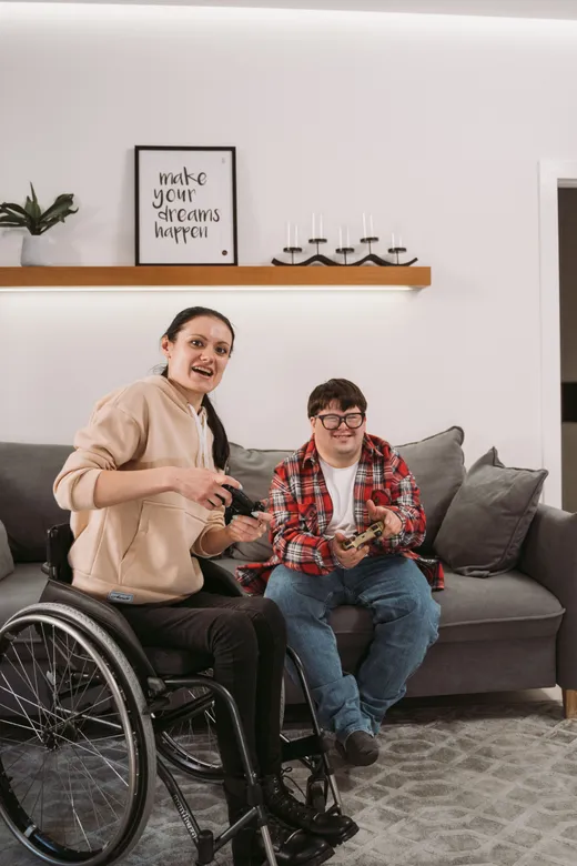 Two young adults relaxing together in a lounge room, one seated in a wheelchair